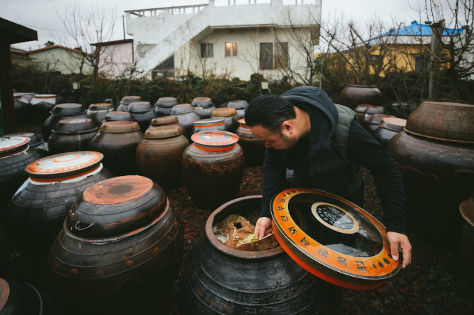 Chef Hooni Kim peers into a clay jar containing Doenjang.  (Photo by Kristin Teig)