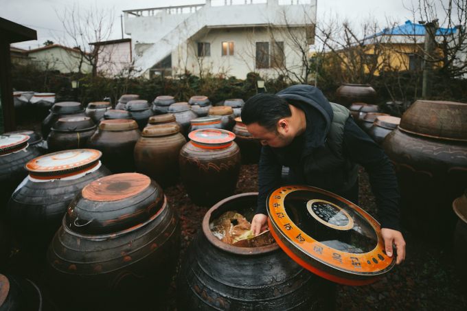 Chef Hooni Kim peers into a clay jar containing Doenjang, one of Korean tradistional mother sauces.  (Photo by Kristin Teig)