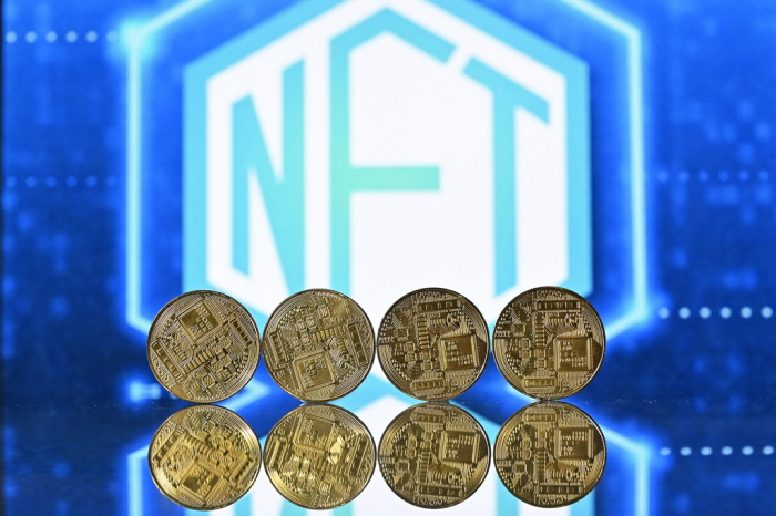 A　photograph　taken　in　London　on　Dec.　30,　2021,　shows　gold-plated　souvenir　cryptocurrency　coins　arranged　by　a　screen　displaying　an　NFT　logo　(Courtesy　of　AFP,　Yonhap)