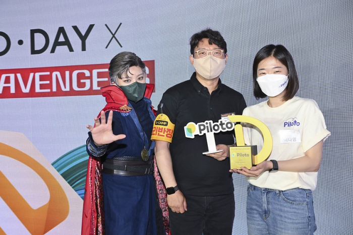 Piloto　founder　Lee　Da-young　(far　right)　wins　the　most　votes　from　judges　and　the　audience　on　D.Day　held　on　May　25.　Lee　poses　with　a　D.Camp　staff　member　and　a　woman　dressed　as　an　Avenger　(Courtesy　of　D.Camp)