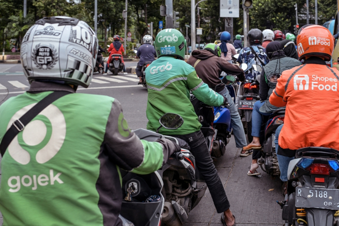 Motorcycle　delivery　drivers　working　for　three　different　online　companies　--　Gojek,　Grab　and　Shopee　--　wait　at　a　traffic　light　in　Jakarta