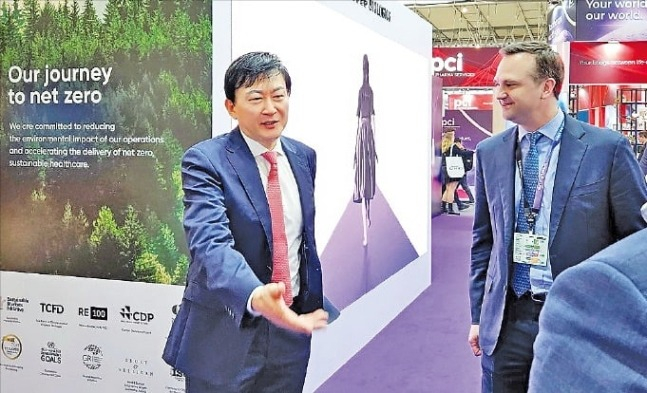 Samsung　Biologics　President　&　CEO　John　Rim　(left)　greets　a　visitor　to　its　booth　at　CPHI　Worldwide　2023,　a　global　bio　and　pharmaceutical　conference,　in　Barcelona　on　Oct.　25,　2023　(Courtesy　of　Samsung　Biologics)