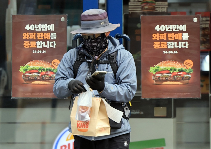 A　customer　buys　food　on　April　8,　2024,　from　a　Burger　King　Korea　outlet　in　Seoul　with　signs　advertising　the　company's　plan　to　stop　selling　the　Whopper　from　April　14,　2024　(Courtesy　of　News1)