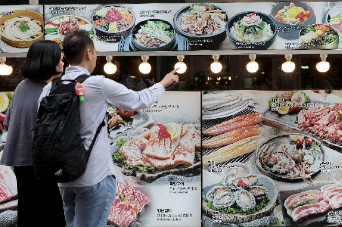 Tourists　in　Myeongdong　look　at　a　restaurant's　menu　display　on　the　window　(Courtesy　of　News1　Korea) 