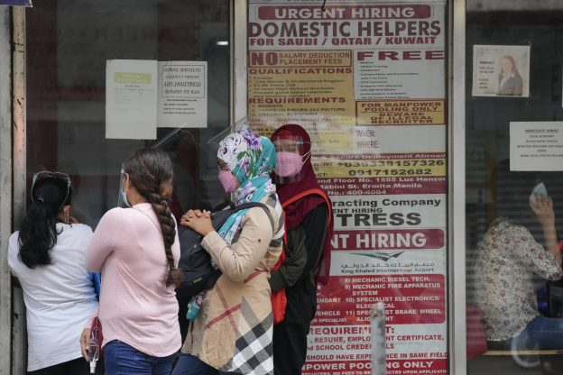 Women　stand　beside　a　sign　advertising　jobs　for　domestic　helpers　to　work　abroad,　outside　an　office　in　Manila　(Courtesy　of　AP　via　Yonhap)
