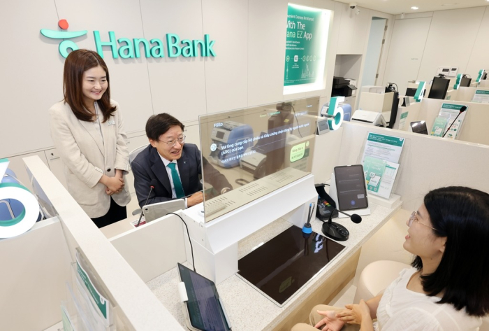 Hana Bank President & CEO Lee Seung-yeul (second from left) speaks with a foreign customer through a transparent display with an artificial intelligence-based real-time interpretation system at its branch dedicated to foreigners in South Korea (File photo by Hana Bank)