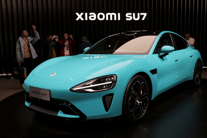 Visitors film Xiaomi's first electric vehicle, the SU7, displayed at an event in Beijing on Dec 28, 2023 (Courtesy of Reuters, Yonhap)