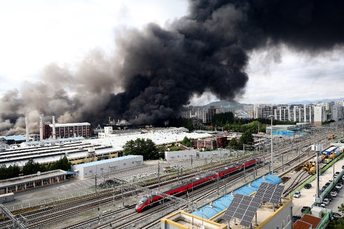 A train moves along nearby tracks as flames engulf Kumho Tire’s Gwangju plant